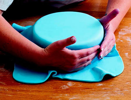 Долонями притискаємо пласт мастики до торту, при цьому акуратно розгладжуючи складки, що утворилися в процесі роботи (пальцями мастику чіпати не можна, щоб зберегти рівну поверхню і не залишити слідів)